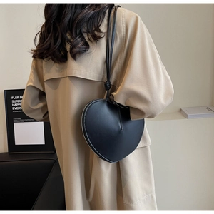 Dettaglio della borsa nera a forma di cuore indossata da una modella in un set moderno