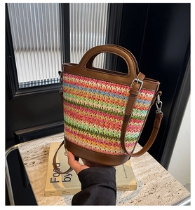 Detail of colorful woven straw bucket bag with dark brown leather trim and handle