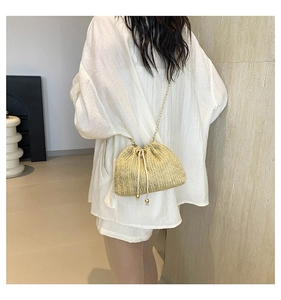Straw woven bucket bag with gold chain strap shown on model in a minimalist setting