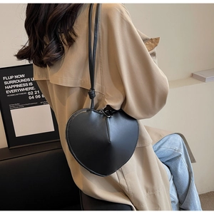 Dettaglio borsa a tracolla nera a forma di cuore indossata con un trench alla moda