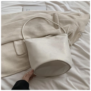 Minimalist white PU leather underarm bucket bag with glossy texture and pearl bow charm