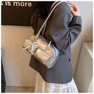 Detail view of silver PU leather handbag with pearl bow pendant and dual flap front pockets