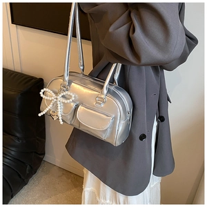 Detail of silver metallic PU shoulder bag with pearl bow and heart pendant on a model