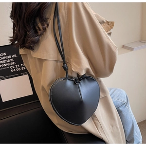 Vista dettagliata di una borsa a tracolla nera a forma di cuore indossata con un cappotto