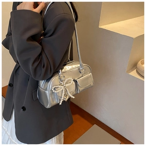 Detail of silver metallic underarm bag featuring pearl bow charm and heart pendant