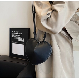 Vista dettagliata della borsa a tracolla nera a forma di cuore su un modello con trench beige