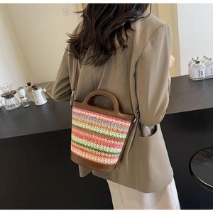 Detail of multi-color woven straw bucket bag with brown leather trim and shoulder strap