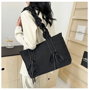Détail du sac cabas en toile noire avec bandoulières à volants et nœuds décoratifs élégants
