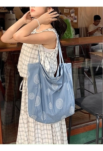 Detail of blue denim tote bag with smiley face pattern shown in a lifestyle cafe setting
