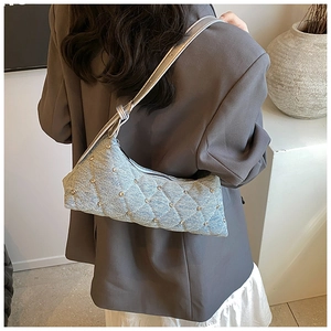 Close-up of light blue denim crescent bag with quilted pattern and metal rivet details