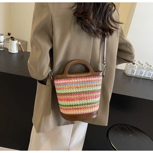Detail of colorful woven straw bucket bag with brown leather trim worn as a crossbody