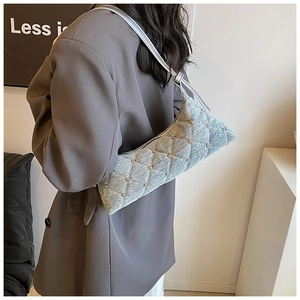Detail of light blue quilted denim baguette bag with gold studs on a grey blazer