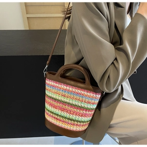 Detail showing colorful straw woven bucket bag with brown leather handles worn by model