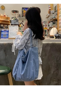 Close-up of blue denim tote bag with light bow print worn in a cafe setting