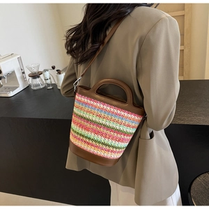 Detail of colorful woven straw bucket bag with brown leather strap and handle design