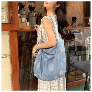 Detail view of light blue denim tote bag featuring white smile patterns in a cafe setting