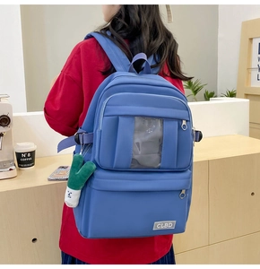 Détail d'un sac à dos en nylon bleu avec poche transparente, couches et pendentif peluche