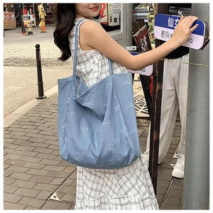 Close-up of denim tote bag with white bow pattern on shoulder for casual daily use