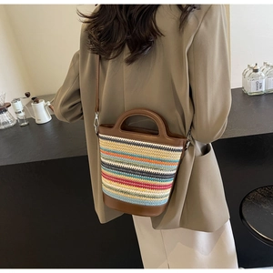 Detail of multi-color striped straw bucket bag with brown leather handles and shoulder strap