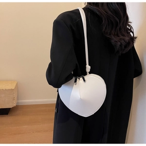 Borsa a tracolla bianca a forma di cuore indossata da una modella in cappotto nero