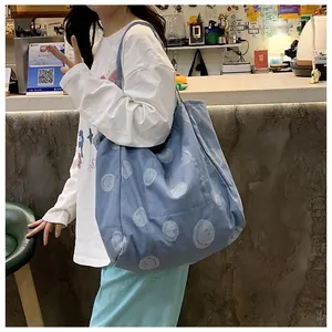 Detailed view of light blue denim tote bag with all-over white smiley face prints