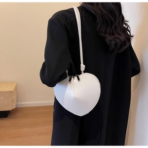 Dettaglio della borsa a tracolla bianca a forma di cuore su una modella in blazer nero