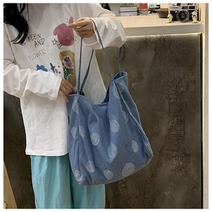 Detailed view of blue denim tote bag with light blue smiley face patterns on a model