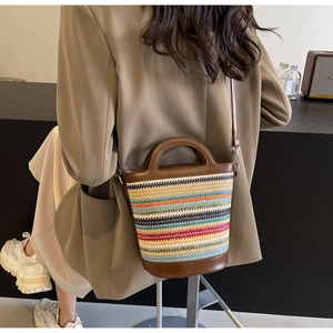 Detail of colorful striped straw bucket bag with brown leather handles and shoulder strap