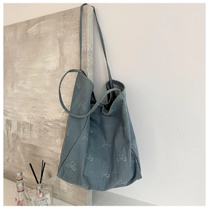 Detailed view of blue denim tote bag featuring light-colored bow patterns in a lifestyle setting