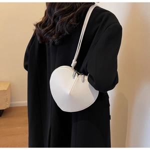 Dettaglio di una borsa a tracolla bianca a forma di cuore abbinata a un cappotto nero