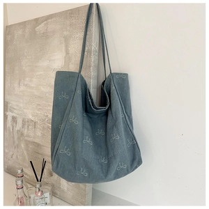 Detailed texture of blue denim tote bag with gray bow prints hanging on a white wall