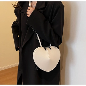 Dettaglio di una borsa a tracolla bianca a forma di cuore indossata con un cappotto