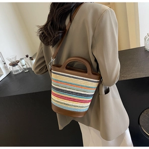 Detail of colorful striped straw bucket bag with brown leather trim worn by model
