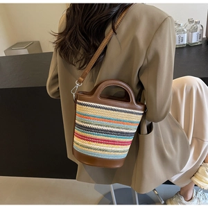 Detail of multi-color woven straw bucket bag with dark brown leather straps and metal hardware