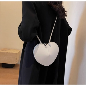 Dettaglio della borsa a tracolla color crema a forma di cuore indossata su un cappotto nero