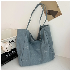 Detail of light blue denim tote bag featuring white bow prints and soft fabric texture