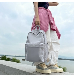 Vista esterna di uno zaino in nylon grigio chiaro con grande tasca frontale vicino al lago