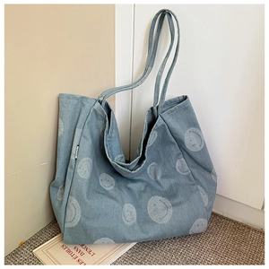 Detail of light blue denim tote bag with white smiley patterns and woven label detail