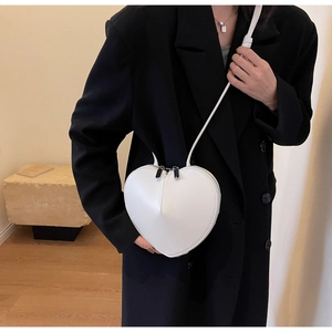 Dettaglio borsa a tracolla a forma di cuore bianca con cerniera argentata su blazer nero