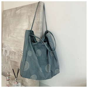 Detail of blue denim tote bag with smiley face pattern hanging on white wall
