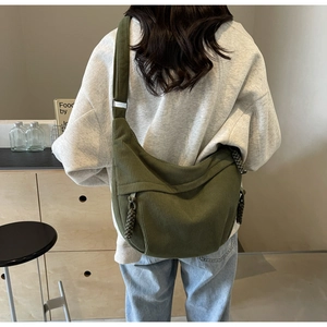 Detail of dark green corduroy crossbody bag featuring a woven rope zipper pull and texture