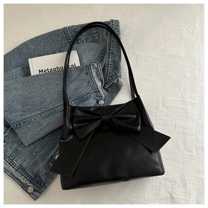 Minimalist black PU leather shoulder bag featuring a large decorative bow on a white surface