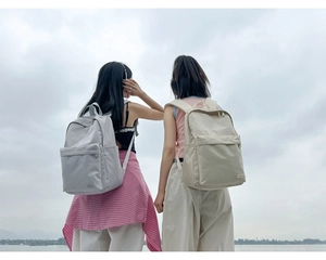 Vista posteriore di due donne con zaini minimalisti in nylon grigio chiaro e beige