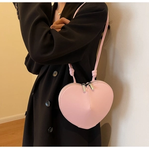 Dettaglio di una borsa a tracolla rosa a forma di cuore indossata su un cappotto nero