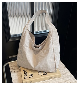Primer plano de un bolso tote de tela crema con bolsillo delantero y correa ancha al hombro