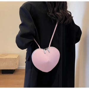 Dettaglio della borsa a tracolla rosa a forma di cuore abbinata a un blazer nero