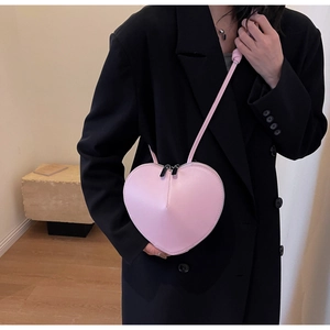 Dettaglio di una borsa a tracolla rosa a forma di cuore indossata su un blazer nero