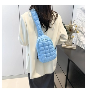 Close-up of light blue quilted puffer crossbody bag with wide strap on a model