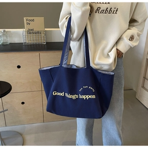 Detailed close-up of dark blue canvas tote bag featuring yellow typography and striped lining