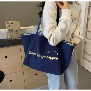 Close-up of navy canvas tote bag featuring yellow artistic lettering and striped lining